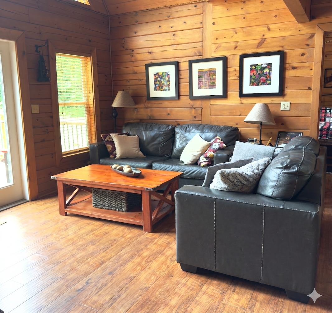 Cozy cabin living room featuring dark leather sofas, a wooden coffee table, and framed artwork on rustic log walls at Circle O Lodge in Marceline Missouri.